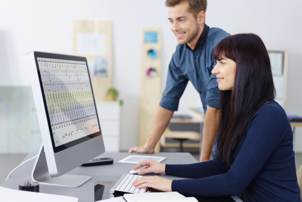 Eine Frau und ein Mann im Büro schauen auf eine Tabelle am pc